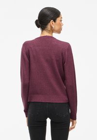 Burgundy sweater with a round neckline, long sleeves, and ribbed hem. Material appears soft and textured, designed for a relaxed fit.
