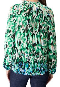 Blouse à manches longues avec col montant, dos plissé et motif léopard abstrait vert, noir, bleu et blanc.
