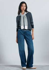 Marinblå randig långärmad tröja med en vit scarf, kombinerad med blå vida jeans och ljusa skor. Mjuka tyger och avslappnad passform.