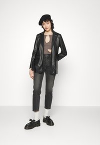Blazer de couro falso preto sobre uma blusa castanha com recorte, jeans escuros de cintura alta e sapatos pretos com sola espessa e atacadores. Meias brancas.