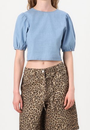 Femme portant un haut court bleu clair à manches bouffantes et un short léopard taille haute arrivant au genou.