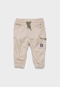 Pantalon en coton beige avec taille élastique, cordon de serrage vert et poche cargo sur le côté, doté de poignets élastiques et d'un patch logo.