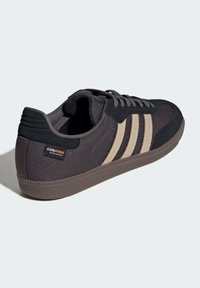 Černá a béžová teniska s texturovaným svrchním materiálem z tkaniny, třemi charakteristickými pruhy a odolnou gumovou podrážkou. Obsahuje značku Cordura.