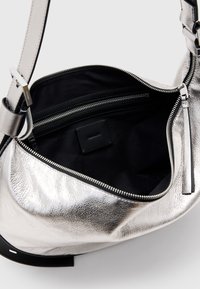 Borsa a spalla metallica argento con superficie testurizzata, dotata di un interno nero, tasca con zip e tracolla regolabile.
