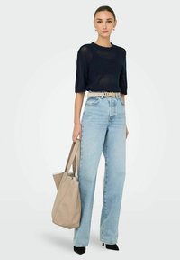 Top lavorato a maglia blu navy con maniche corte, jeans azzurri a vita alta, borsa beige a tracolla e scarpe col tacco nere. Sfondo neutro.