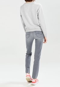 Felpa grigia, jeans skinny grigi chiari e sneaker a righe rosa. Vista da dietro, che mostra la vestibilità e la texture del capo.