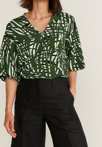 Blusa a righe verdi e bianche con scollatura a V, maniche corte a palloncino, abbinata a pantaloni neri a vita alta. Tessuto liscio, vestibilità comoda.