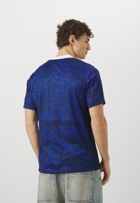 Camicia blu a maniche corte con un motivo testurizzato, caratterizzata da dettagli rossi. Collo e maniche bianchi, realizzata in tessuto leggero.