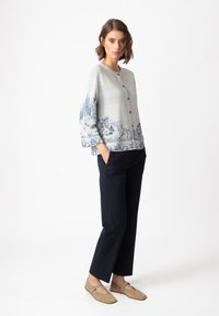 Light gray cardigan with blue scenic print, round neckline, and button closure. Paired with dark pants and beige flats. Smooth texture.