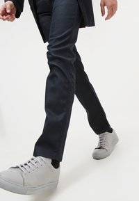 Mörkblå, slim-fit jeans i denim, kombinerat med ljusgrå sneakers med texturerad finish och platta gummisulor.