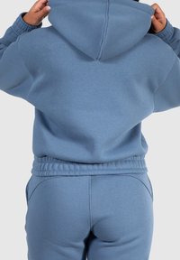 Sudadera azul claro con puños y cintura elásticos, hecha de una tela suave. Presenta una capucha forrada y un corte relajado. Se lleva con pantalones a juego.