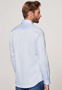 Camisa de manga larga azul claro con cuello clásico, textura suave y ajuste entallado, con puños de botón y dobladillo curvado.