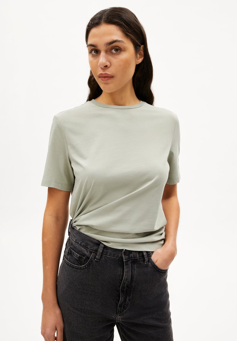 Hellgrünes T-Shirt mit kurzen Ärmeln aus glattem Stoff, mit Rundhalsausschnitt und lockerer Passform, kombiniert mit dunkler Denim-Jeans.