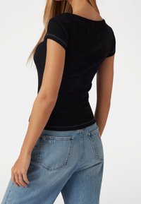 Top corto de manga corta negro acanalado combinado con jeans azul claro de talle alto, con un corte clásico y detalles sutiles de costura.