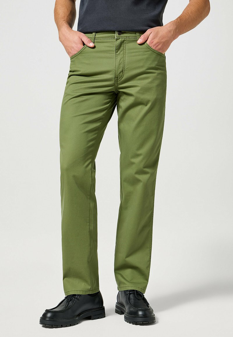 Groene katoenen broek met een rechte snit, voorzien van voorzakken en een ritssluiting aan de voorkant. Gemaakt met zwarte schoeisel, wat zorgt voor een casual look.