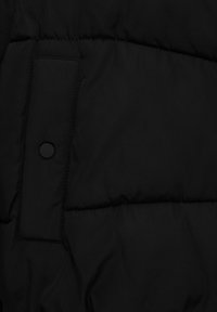 Black puffer jacket fabric featuring a smooth texture, visible stitching, and a snap button accent near a rectangular pocket.