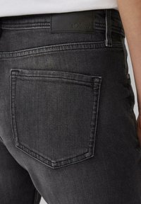 Czarne dżinsy z denimu z tylną kieszenią o prostym designie, teksturowaną powierzchnią materiału i naszywką z logo s.Oliver nad paskiem.