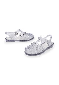 Sandalias de gel transparentes con recortes circulares, tachuelas en tono plateado y una correa trasera para soporte. Suela plana y diseño abierto para una mayor transpirabilidad.