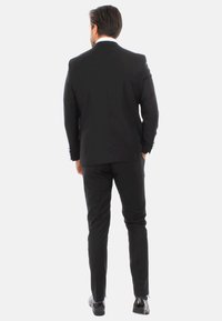 Completo nero con una vestibilità su misura, giacca a un bottone e pantaloni slim. Tessuto liscio e linee pulite. Scarpe in pelle con una lucentezza discreta.