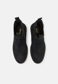 Chaussures noires en daim à enfiler avec des panneaux latéraux élastiques et une semelle en caoutchouc, présentant un design minimaliste et une texture lisse.