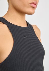 Black ribbed tank top with a round neckline, featuring a small black Nike logo on the chest and sleeveless design. Smooth texture.