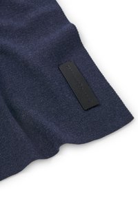 Granatowa dzianina o gładkiej fakturze, z czarną prostokątną metką wytłoczoną z napisem "Adolfo Dominguez" z jednej strony.