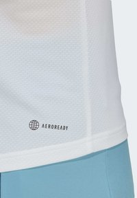 Balta tekstūruota sportinė marškinėliai su AEROREADY logotipu apatiniame krašte, derinami su šviesiai mėlynomis šortais, pabrėžiantys šiuolaikišką pjūvį ir funkcinį dizainą.