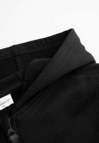 Czarna bluza z suwakiem, z miękką podszewką, zaokrąglonym kołnierzem i gładką teksturą materiału. Etykieta widoczna w środku.