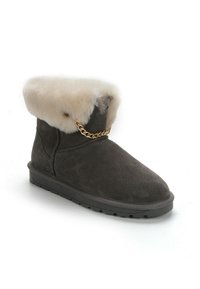 Stivale alla caviglia in suede grigio con un morbido risvolto in pelliccia beige, accentato da una catena dorata sul davanti e una suola in gomma nera con battistrada.