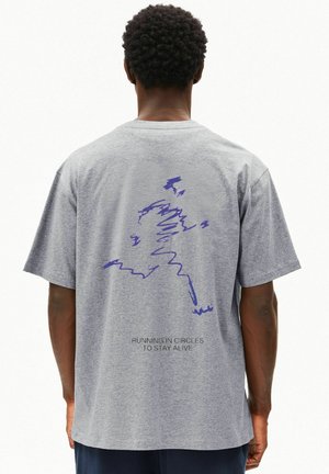 Person trägt ein graues T-Shirt mit einem blauen abstrakten Läuferdesign und dem Schriftzug „RUNNING IN CIRCLES TO STAY ALIVE“ auf dem Rücken.