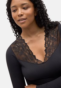 Prenda negra de manga larga con escote en V pronunciado y detalles de encaje floral en el cuello, textura suave y diseño ajustado.