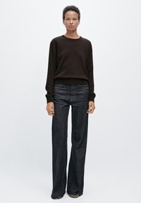 Brązowy sweter z długimi rękawami i prążkowanymi mankietami, połączony z ciemnymi, szerokimi spodniami dżinsowymi. Prosty design i neutralna paleta kolorów.
