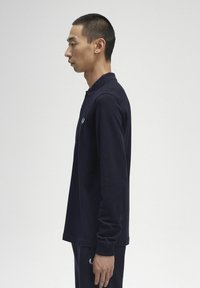 Tumesinine pikakäistega polo särk kraega, millel on rindkerel peen logo ja soonikkoes varrukas. Siluge tekstuur ja mugav lõige.