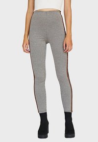 Leggings de cintura alta con un estampado a cuadros en blanco y negro, que cuentan con franjas laterales en marrón que contrastan y un ajuste ceñido. Tejido texturizado.