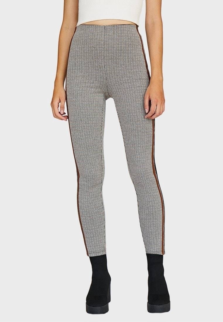 Leggings de cintura alta con un estampado a cuadros en blanco y negro, que cuentan con franjas laterales en marrón que contrastan y un ajuste ceñido. Tejido texturizado.