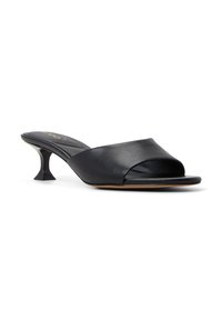 Mule de cuero negro abierto en la parte delantera con una tira ancha y un tacón escultural único. Textura suave, diseño minimalista y detalle del logo en dorado en la plantilla.