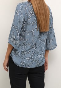 Blusa azzurra con motivo botanico, dotata di maniche a tre quarti morbide e di una vestibilità rilassata, realizzata in un tessuto testurizzato.