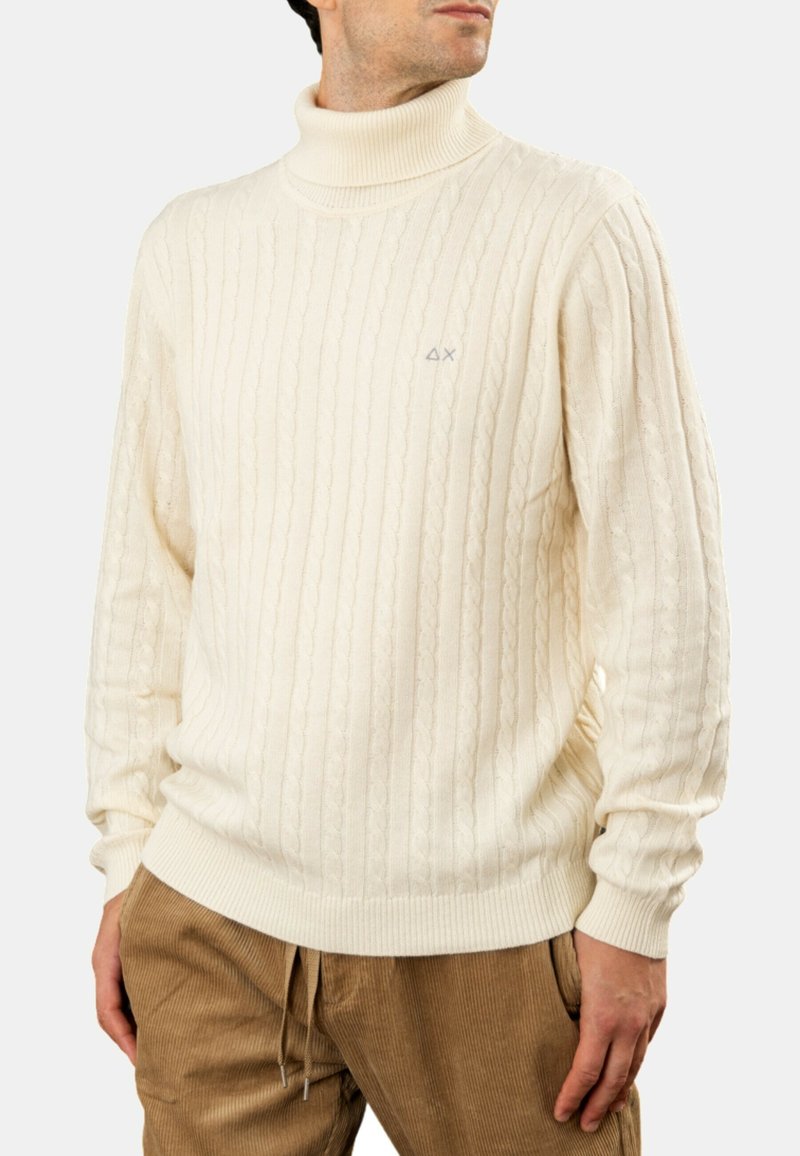 Maglione a collo alto lavorato a maglia a treccia di colore crema, realizzato in un tessuto morbido, con polsini e orlo a coste, e un piccolo logo sul petto.