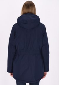 Jachetă cu glugă de culoare bleumarin, cu talie strânsă, mâneci lungi și o margine curbată. Fabricată dintr-un material neted, rezistent la apă.