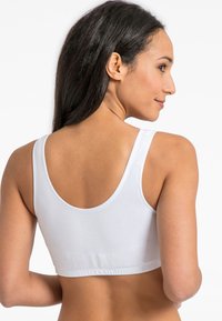 Balta sportinė liemenėlė su plačiomis petnešėlėmis, apvali nugaros iškirpte ir prilipusiu dizainu. Pagaminta iš lygaus, tampri, be siūlių audinio.