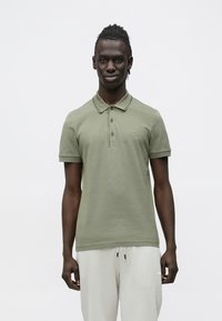 Oliwkowo-zielona koszulka polo z klasycznym kołnierzykiem, krótkimi rękawami i subtelnym logo. Wykonana z przewiewnej bawełnianej mieszanki.