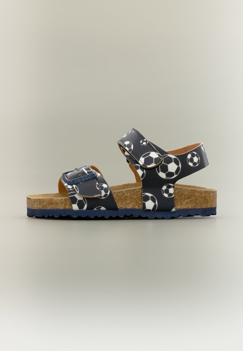 Παιδικό μπλε σαγιονάρι με λευκό σχέδιο ποδοσφαιρικής μπάλας, πάτο από φελλό, δύο ρυθμιζόμενα λουριά με αγκράφες και μπλε καουτσούκ σόλα.