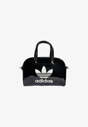 Sac à main Adidas noir brillant avec deux poignées, fermeture éclair, et grand logo trèfle blanc accompagné de texte sur le devant.