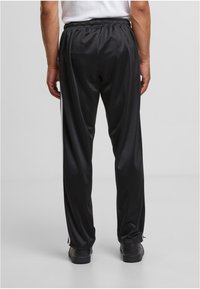 Crne, elegantne trenirke s elastičnom gumom u struku, bočnim trakama i glatkom teksturom. Imaju opušteni kroj i rebraste manžete na gležnjevima.