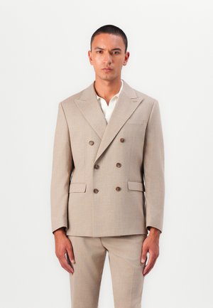 Beige double-breasted suit with two buttons, notch lapels, side pockets, and matching trousers; fabric appears smooth with a subtle texture.