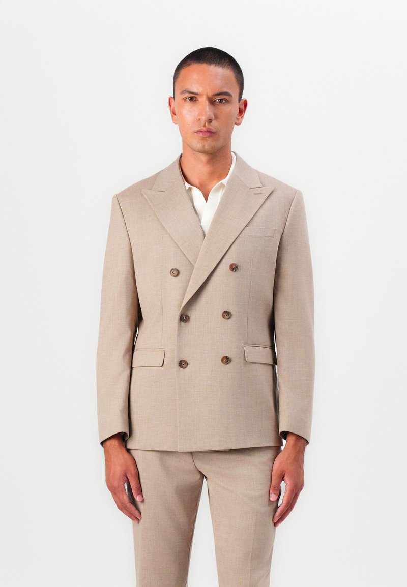 Beige double-breasted suit with two buttons, notch lapels, side pockets, and matching trousers; fabric appears smooth with a subtle texture.
