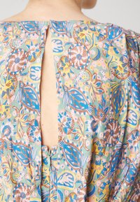 Kledingstuk met bloemenpatroon in pastelkleuren, voorzien van een keyhole achterkant met een ritssluiting. De stof is lichtgewicht met een zachte textuur.