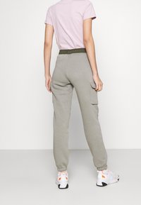 Šedé tepláky s volným střihem, elastickým pasem a bočními kapsami. Oblečené s růžovým tričkem a bílými teniskami.