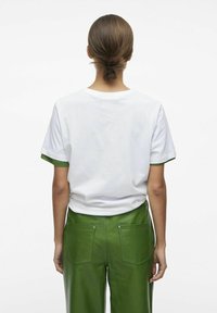 Hvid bomulds T-shirt med grønne accenter på ærmerne, parret med grønne læderbukser med to baglommer og synlige hardware-detaljer.