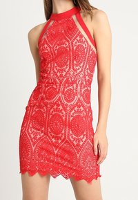 Abito rosso in pizzo con un motivo intricato, scollatura all'americana e orlo smerlato. Tessuto trasparente con silhouette aderente e colore vivace.